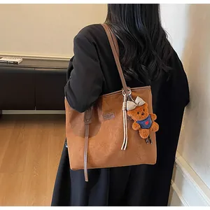 Detailansicht einer braunen Wildleder-Tragetasche mit Plüschbärenanhänger auf einem Model