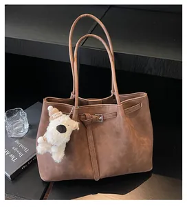 Detalle de bolso tote marrón oscuro con hebilla de cinturón y un peluche sobre mesa negra