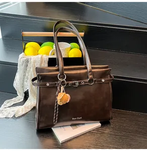 Detail of dark brown leather tote with decorative buckle and baseball charm accessory