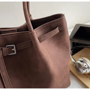 Detalle del bolso tote de ante marrón café con hebillas plateadas y textura de asa