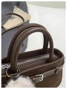 Close-up of brown bucket bag with plush white pompom and silver metal zipper detail