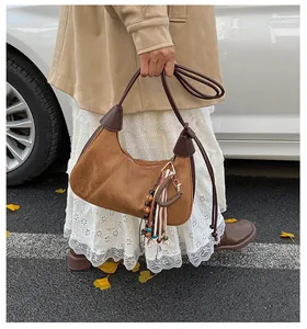 Détail du sac demi-lune en daim marron avec pendentif ethnique à pompons et bords cuir