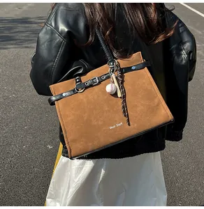 Detail of a large brown suede tote bag with black straps and baseball bag charm