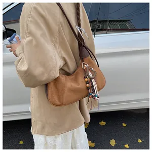 Détail du sac croissant en daim marron avec pompons bohèmes et perles colorées sur le côté