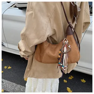 Détail du sac selle en daim marron avec pompons bohèmes et style automnal élégant