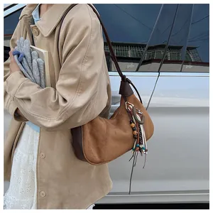 Détail du sac demi-lune en daim marron foncé avec pompon ethnique perlé et lanière en cuir