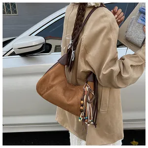 Détail d'un sac hobo en daim marron avec des franges et des perles de couleur sur un mannequin