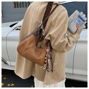 Détail d'un sac hobo en daim marron avec pendentif à franges bohème porté par un mannequin