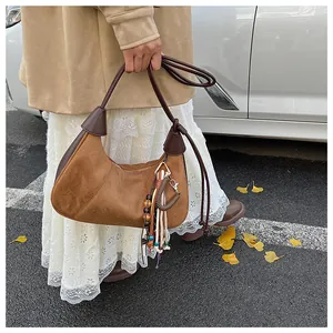 Détail d'un sac demi-lune en daim marron avec pompon coloré dans un décor d'automne