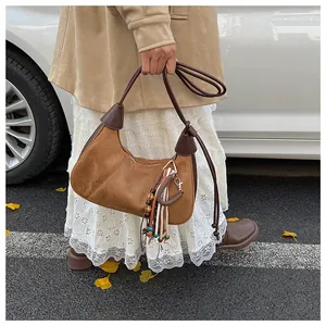 Détail du sac croissant en daim marron avec pompons bohèmes et breloque en perles
