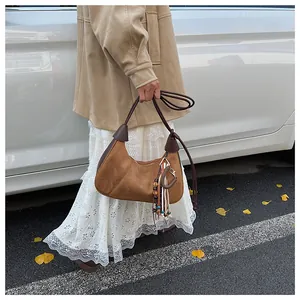 Sac hobo en daim marron avec pompon en perles devant une voiture blanche et feuilles d'automne