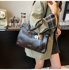 Detail of dark brown tote bag in glossy faux leather with baseball charm and white text
