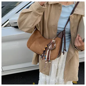 Gros plan du sac croissant en daim marron avec pompon bohème et détails de perles