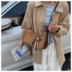 Sac bandoulière en daim marron avec pompons bohèmes et perles colorées porté par un mannequin