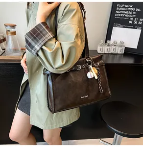 Detail view of a large brown leather tote bag with white logo and sports charm