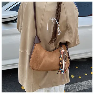 Détail du sac hobo en daim marron avec pendentif ethnique porté sur un manteau camel