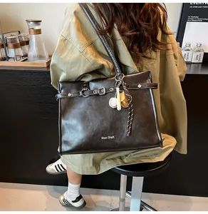 Detail of a large brown tote bag with metal buckles and a baseball bat charm ornament