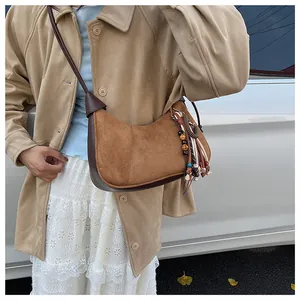 Détail d'un sac hobo en daim marron avec pompon ethnique et finitions en cuir lisse