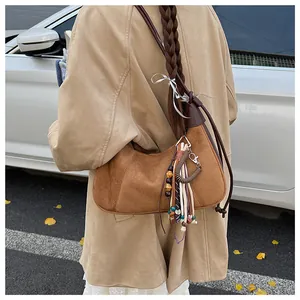 Sac hobo en daim marron avec pendentif ethnique porté sur un long manteau crème
