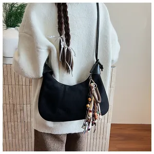 Détail d'un sac demi-lune en daim noir avec pompons de perles colorées et fine bandoulière