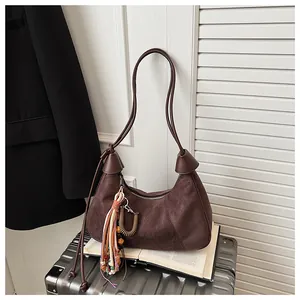 Détail du sac demi-lune en daim marron foncé avec pompon ethnique posé sur un livre