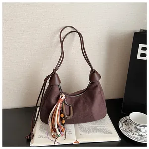 Détail du sac demi-lune en daim marron café avec des breloques à pompons sur un livre