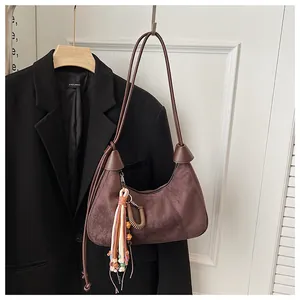 Détail du sac hobo en daim marron foncé avec pompon coloré et accessoire en spirale décoratif