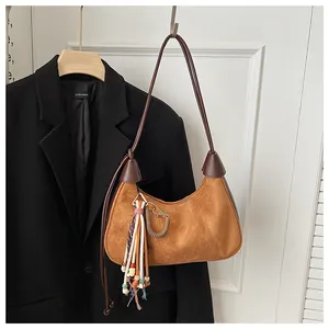 Détail d'un sac hobo en daim marron avec des charms ethniques sur un blazer noir