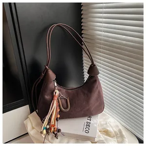 Gros plan du sac hobo en daim marron avec pompon en perles et détails métalliques