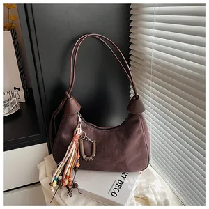 Détail du sac à bandoulière en daim marron foncé avec pompons colorés et pendentif en bronze