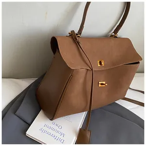Detail view of the brown suede handbag featuring dual metal twist locks and accordion sides