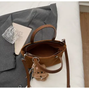 Detail of caramel suede bucket bag with top handles, slim strap and cute plush dog charm