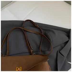 Macro detail of brown suede crossbody bag featuring elegant gold rectangular metal twist lock