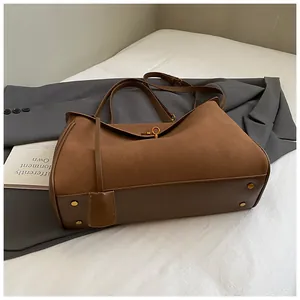 Brown suede tote bag with golden lock and smooth leather trim on a white textile surface