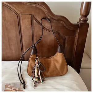 Détail du sac en daim marron avec nœud tressé et pompons colorés aux perles