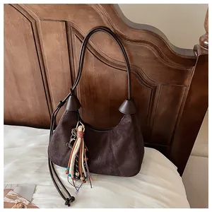 Détail du sac hobo en daim marron foncé avec pompons ethniques et bandoulière en cuir