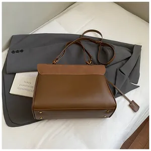 Detail view of the brown trapezoid tote bag showing matte leather texture and gold metal feet