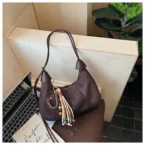 Détail d'un sac demi-lune vintage en daim marron foncé avec pendentif à pompon décoratif