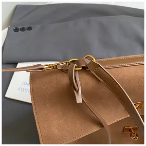 Detail of brown suede shoulder bag featuring a gold metal buckle and vintage texture