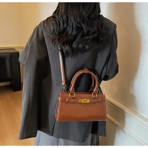 Détail d'un sac à main en cuir marron avec fermoir doré, poignée et bandoulière réglable