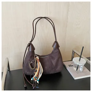 Détail d'un sac hobo en daim marron avec un pendentif à franges bohème et coloré