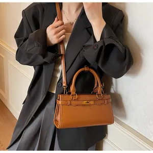 Sac bandoulière en cuir caramel avec fermoir rotatif doré porté sur un blazer noir