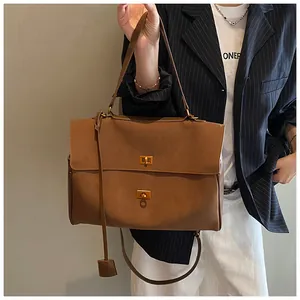 Detail of a brown matte leather tote bag with dual gold twist locks and decorative tag