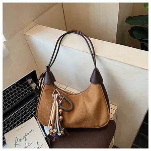 Détail du sac croissant en daim marron avec breloque à franges sur une chaise