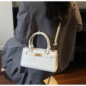 Sac bandoulière chic en cuir blanc crème porté avec un costume gris dans un intérieur