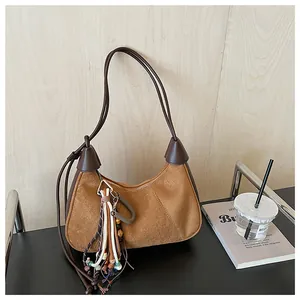 Détail du sac hobo en daim marron avec pompon ethnique et bandoulière en cuir