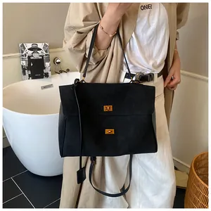 Detail of black suede tote bag with dual gold twist locks and adjustable shoulder strap