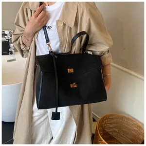 Detail of black tote bag featuring gold lock and buckle hardware on matte leather