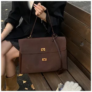 Close-up of a brown suede tote bag featuring gold twist locks and leather hangtag detail