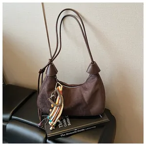 Détail du sac demi-lune en daim marron foncé avec pompon en perles colorées et sangle